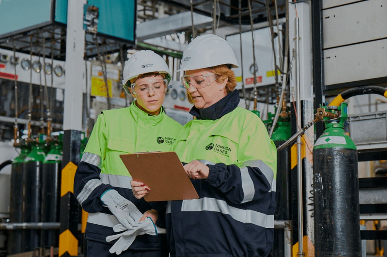 Dos profesionales de Nippon Gases revisando procesos de eficiencia operativa en planta, representando la competitividad y el talento en la industria española.